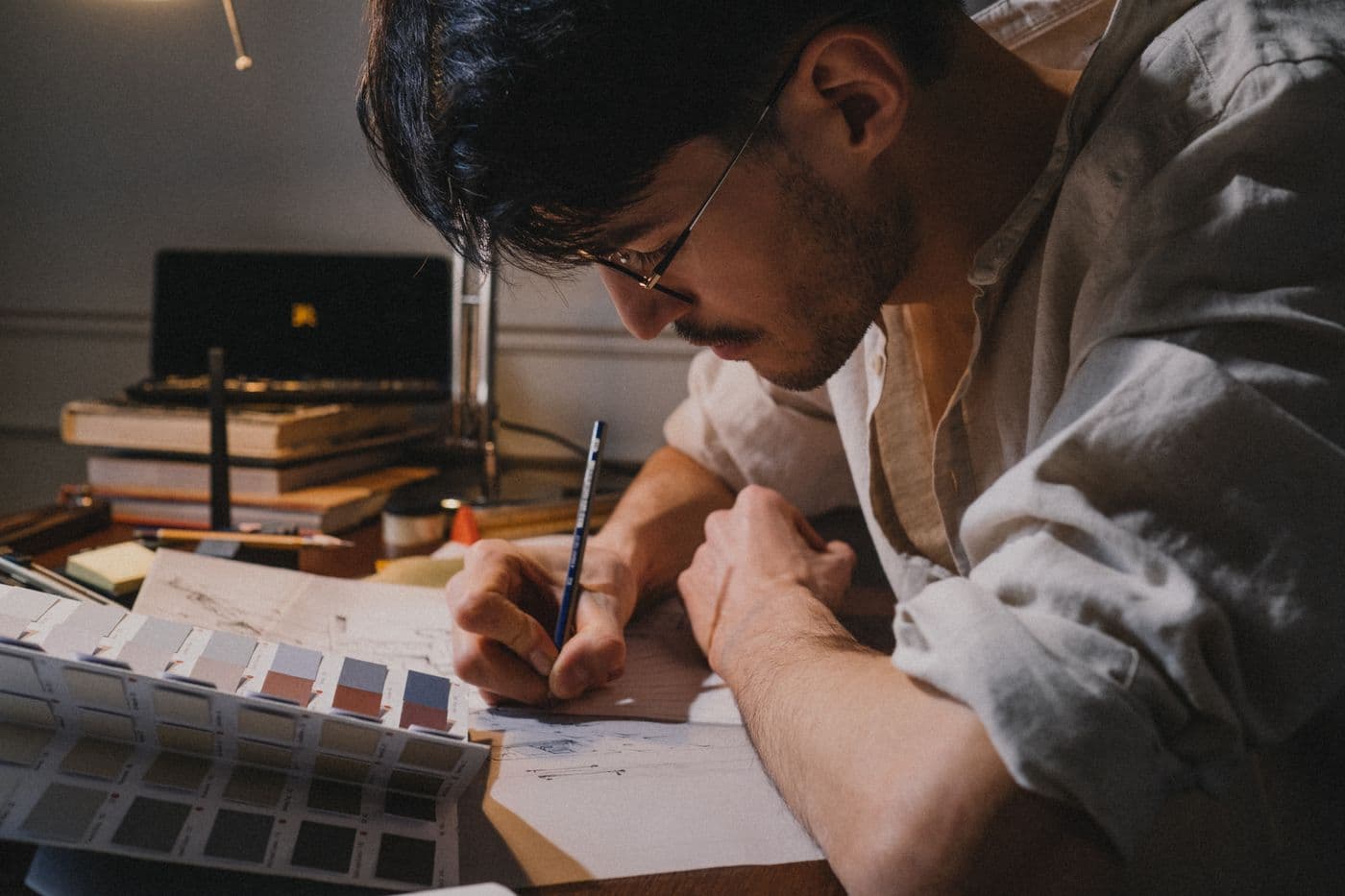 A person drawing at their desk under a single lamp.